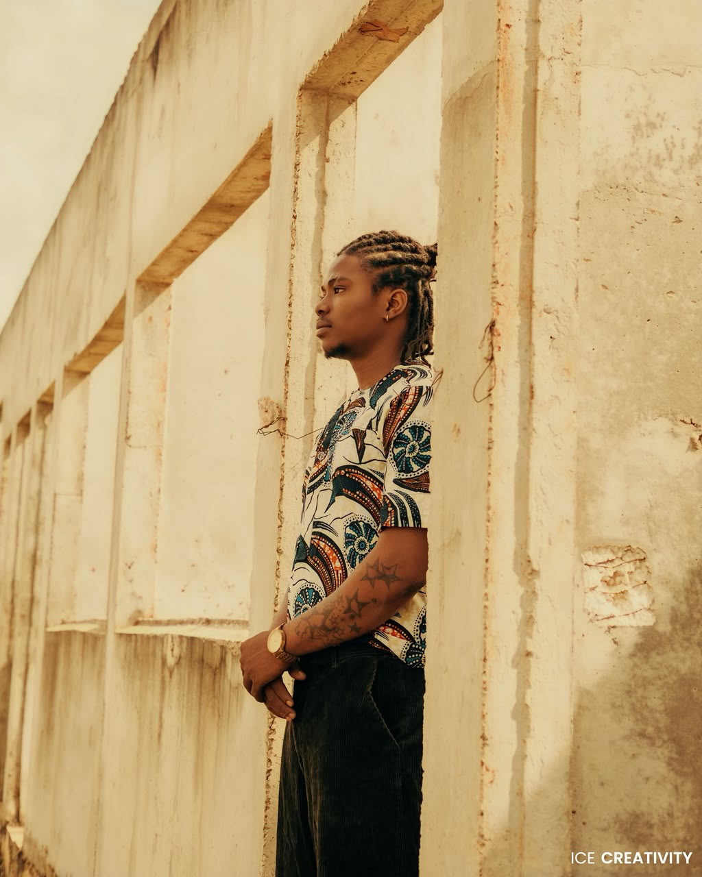OIM THUG en chemise à motifs, de profil contre un mur ocre